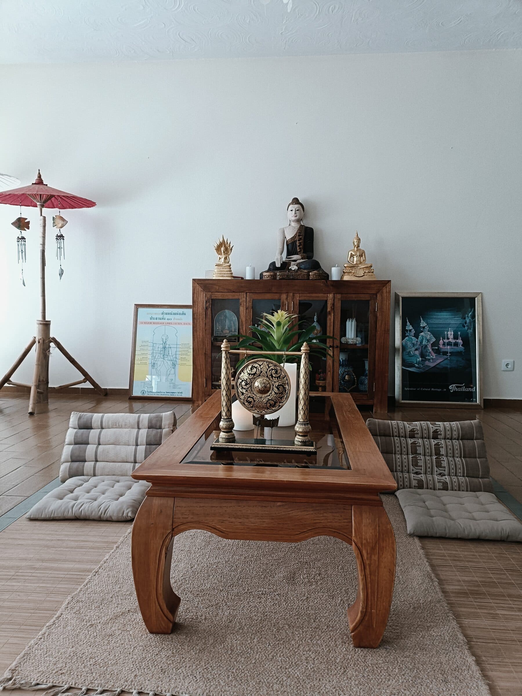 A corner with Buddha statues, a ceremonial gong, and framed Thai art
