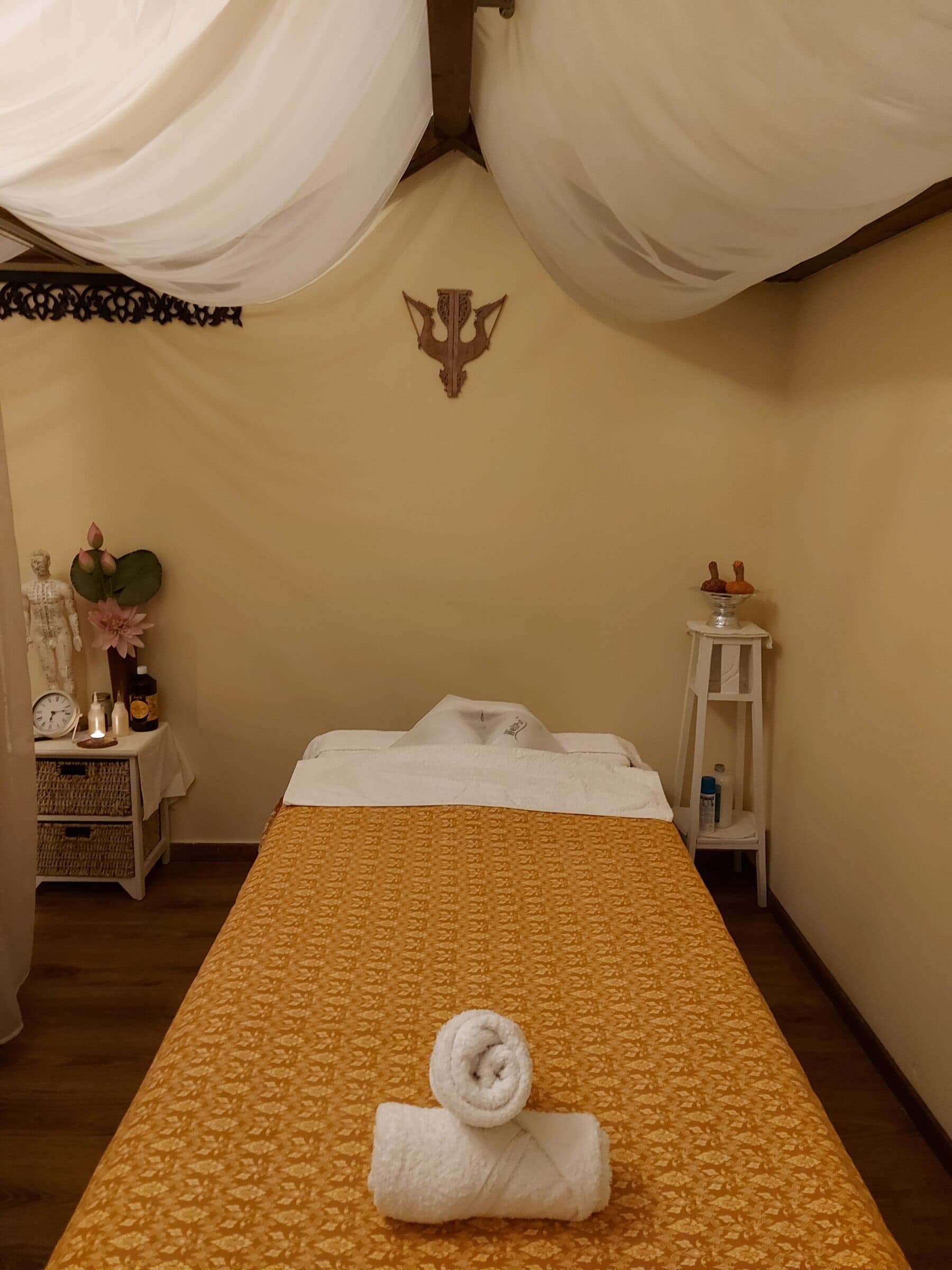 A treatment room with canopy drapes, warm linens, and rolled towels