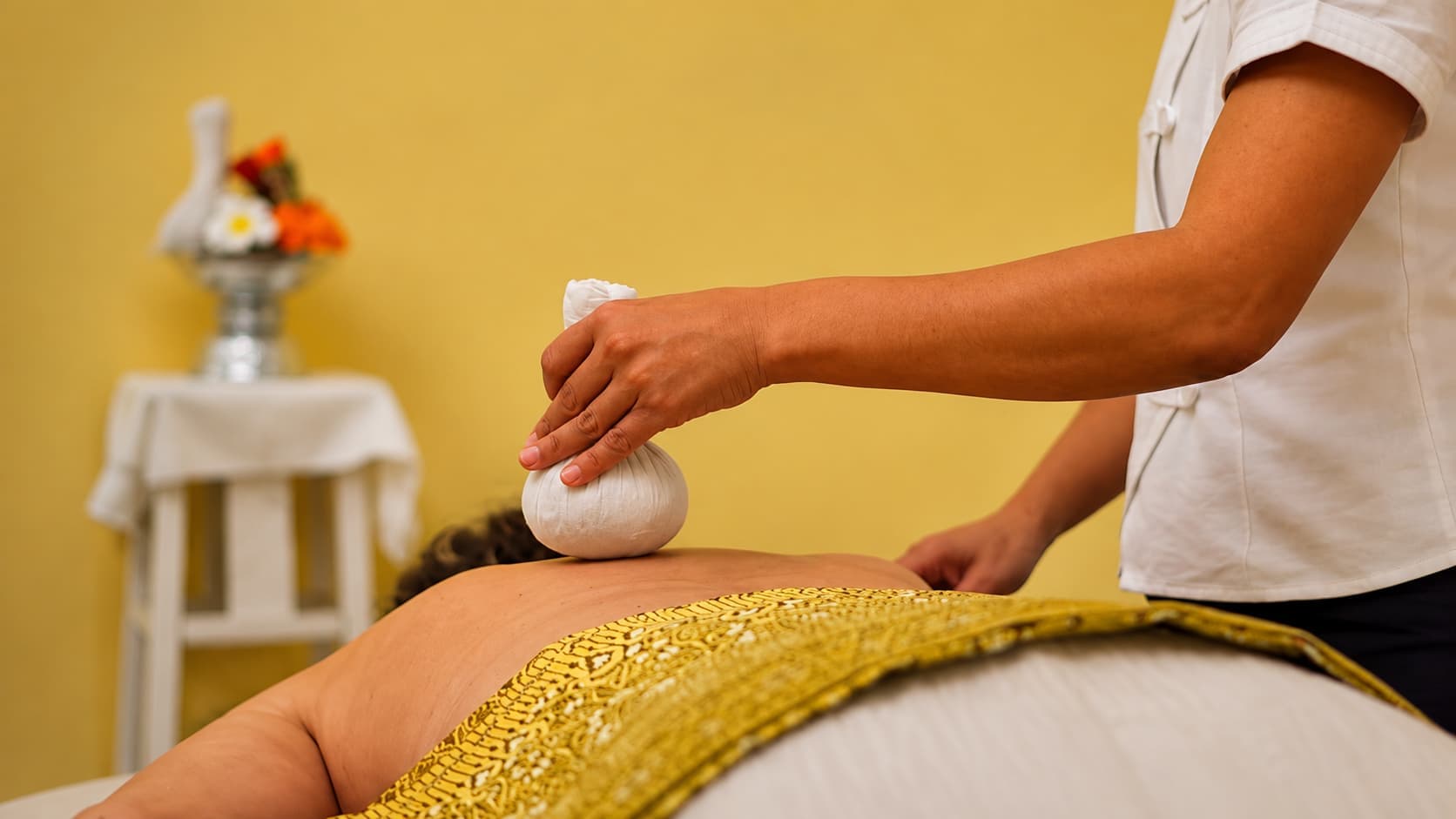 A therapist applying a warm Thai herbal compress during a traditional Thai massage treatment