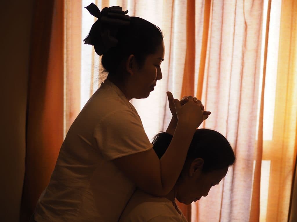 A therapist cupping a seated guest's head during a traditional Thai massage