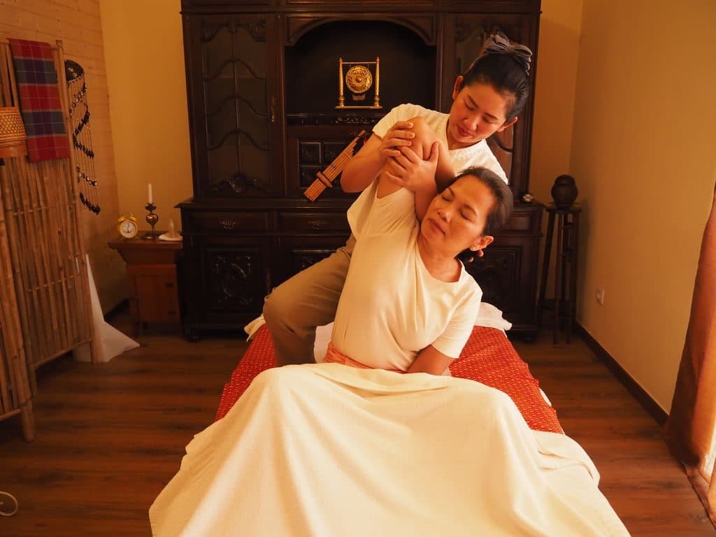 A therapist working a seated guest's shoulder and neck during a traditional Thai massage